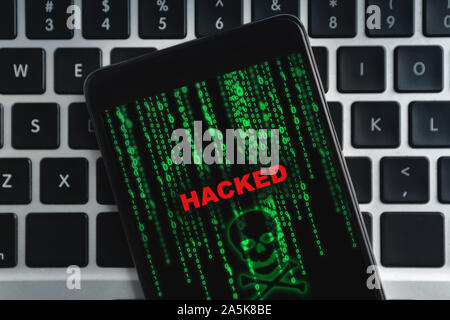 Primo piano dello smartphone hackerato giacente sulla tastiera del notebook Foto Stock