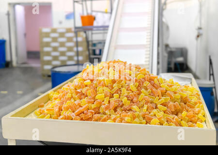 Ready-made gocce di gomma si trova su un vassoio in corrispondenza di una fabbrica dolciaria contro lo sfondo di una sfocata interno di un workshop con un nastro trasportatore Foto Stock