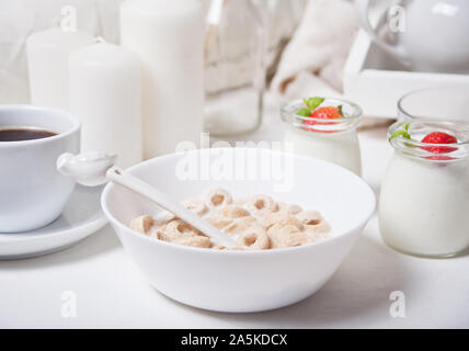 Deliziosi e nutrienti loop di cereali in una ciotola con il latte per la sana prima colazione per i bambini con yougurt in vasetti sullo sfondo Foto Stock