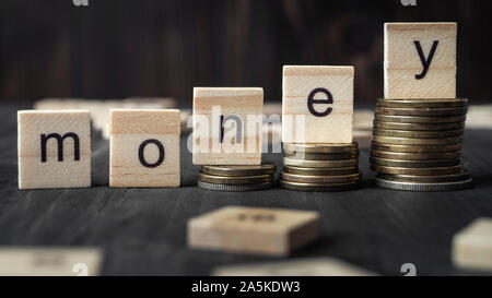 Le monete sulla pila di scale come fase crescente crescita e cubo di legno blocco con parola denaro, close up Foto Stock