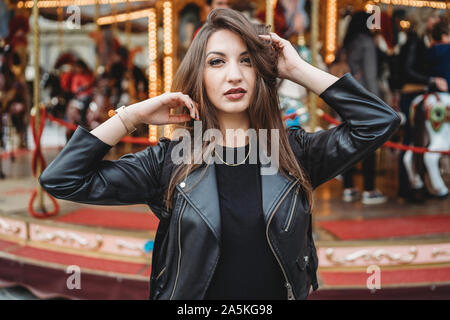 Donna di toccare i capelli e in posa di fronte della giostra Foto Stock