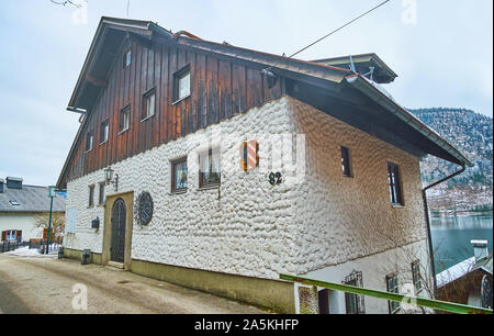 HALLSTATT, Austria - 25 febbraio 2019: storica casa alpina con tetto in legno e i muri in pietra, coperto con intonaco bianco, il 25 febbraio in Hallta Foto Stock