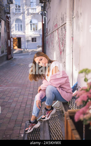 Alla moda ed elegante alla moda giovani ragazze in bianco T-shirt, jeans, accogliente maglia rosa maglione posingin la città. Foto Stock