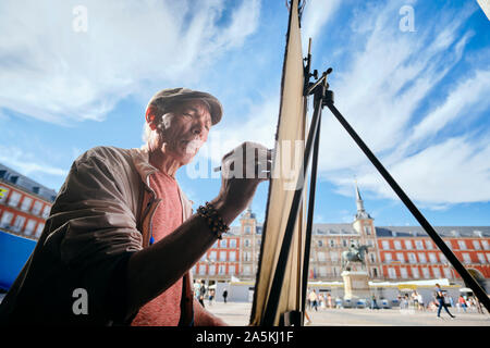 Maschio maturo artista di strada disegno su tela in town square, Madrid, Spagna Foto Stock