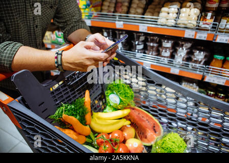 Uomo con lo smartphone fare shopping nel negozio di alimentari Foto Stock