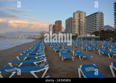 Righe di vuoto azzurro di sedie a sdraio e ombrelloni sulla spiaggia Playa de Levante Beach, molto presto su una domenica mattina di ottobre, Benidorm, Provincia di Alicante, Spagna Foto Stock