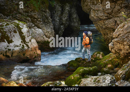 Trekker femmina si erge su una roccia ricoperti di MOSS nel canyon del fiume, Kamniska Bistrica, Slovenia Foto Stock