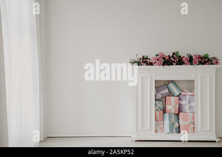 Caminetto bianco con fiori e regali all'interno della camera bianca Foto Stock