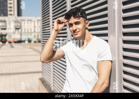 Per il tempo libero all'aria aperta. Elegante guy standing sulla strada Pendente ritornare decollare occhiali da sole cercando riposo gioiosa Foto Stock