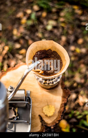 Erogazione di caffè di gocciolamento in giardino. Mano versando acqua calda dal bollitore sopra la polvere di caffè. Foto Stock