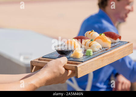 Delizioso sushi servita e trattenuto dalle mani di un uomo con sfondo non focalizzato. Foto Stock