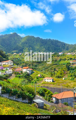 Villaggio pittoresco Porto da Cruz in Madeira, Portogallo. Piccola città circondata da verdi colline. Gli edifici rurali su una collina. Zona remota del paesaggio portoghese. Bellissimo paesaggio. Foto Stock