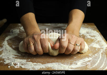 La preparazione tradizionale di pasta fatta in casa. Vista ravvicinata della donna le mani per impastare la pasta fresca per la produzione di pane o pizza su un tavolo infarinato Foto Stock