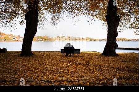 Coppia seduta su una panchina circondata da foglie di autunno godere un paesaggio Foto Stock
