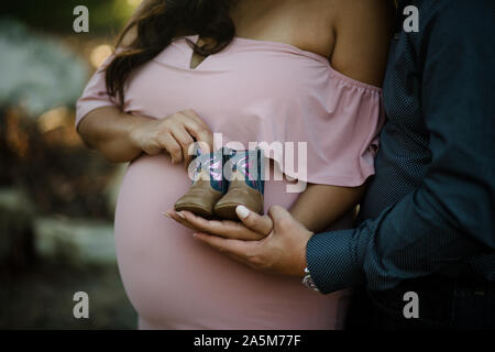 Giovane Azienda Stivali bambino nella parte anteriore del baby bump Foto Stock
