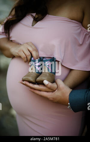 Giovane Azienda Stivali bambino nella parte anteriore del baby bump Foto Stock