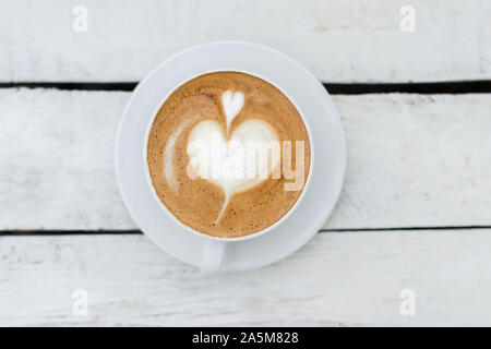 Bianco grande tazza di caffè con il cuore a forma d'arte bianca sul tavolo di legno con copia spazio. Foto Stock