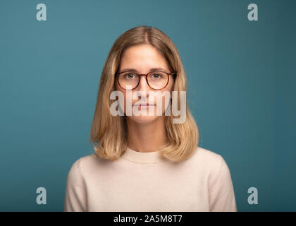 Ritratto di una bionda imprenditrice con gli occhiali di fronte a sfondo blu Foto Stock