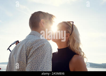 Coppia giovane Kissing contro il sole in spiaggia Foto Stock
