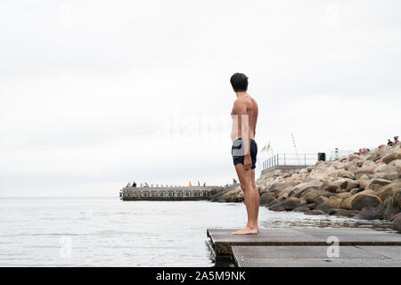 Uomo in piedi sul Boardwalk prima di nuotare Foto Stock