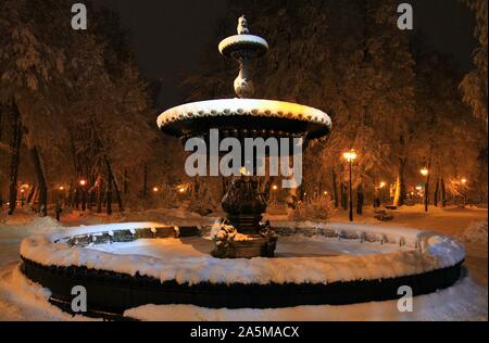 Kiev, Ucraina - 14 dicembre 2018: antica fontana ricoperta di neve. Inverno o Mariinsky Khreshcatyi parco sotto l'illuminazione notturna Foto Stock