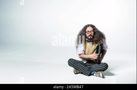 Ritratto di un ragazzo da stupidi tenendo una valigetta e seduto sul pavimento bianco Foto Stock