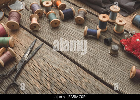 Vintage elementi di cucitura: forbici, ditale, legno rocchetti di filato, cuscino per pin compresi, aghi. Vista dall'alto. Copia spazio per il testo. Foto Stock