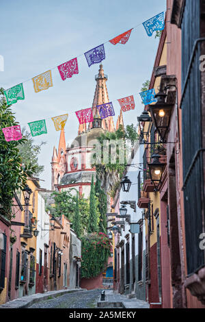 Le cupole e le guglie della Parroquia San Miguel Arcangel chiesa visibile attraverso il banner di carta chiamato papel picado su Aldama Street nel quartiere storico di San Miguel De Allende, Messico. Foto Stock