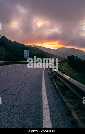 Vuoto bordo stradale su un paesaggio di montagna con orange burning cloudscape sunrise paesaggio Foto Stock