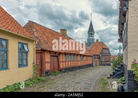 In ciottoli di vecchio-street con un rosso casa in legno e muratura e il municipio in background, Ebeltoft, Danimarca, 9 settembre 2019 Foto Stock