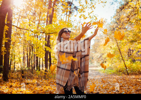 Caduta stagione attività. Donna gettando le foglie in autunno foresta al tramonto. Giovane donna avendo divertimento all'aperto indossare abbigliamento elegante Foto Stock