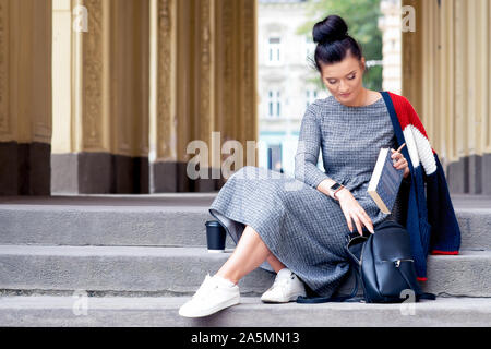 Donna giovane studente è mettere i libri in zaino nero sulle scale. Ragazza dello studente è mettere un libro in uno zaino sulle scale. Il concetto di istruzione. Foto Stock