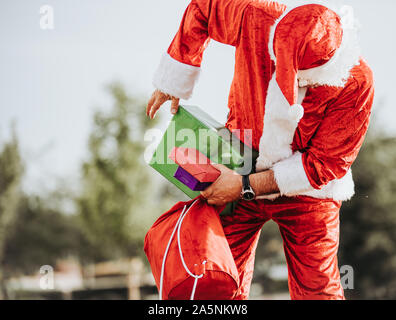 Foto di stock di Babbo Natale senza barba mettendo in piedi presenta in un sacchetto rosso. Il tempo di Natale Foto Stock