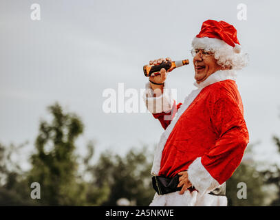 Foto di stock di profilo di Babbo Natale senza barba di bere una birra. Il tempo di Natale Foto Stock