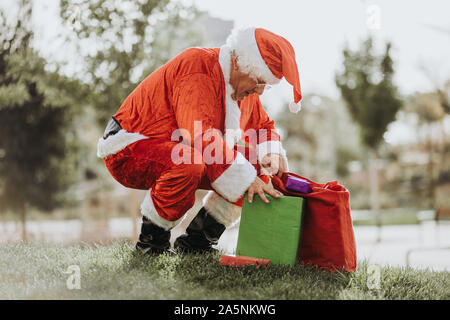 Foto di stock di Babbo Natale senza barba mettendo in piedi presenta in un sacchetto rosso. Il tempo di Natale Foto Stock