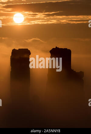 Il sole sorge alle spalle di una nebbia copriva Corfe Castle nel Dorset. Foto Stock