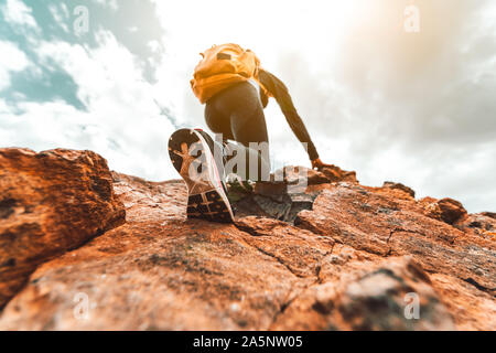 Donna escursionista con zaino è arrampicata in montagna rocciosa. Focus sulla scarpa Foto Stock