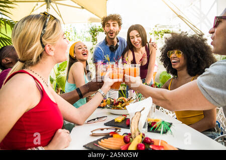 Gruppo di felice multirazziale amici divertendosi e bere cocktail di tostatura. Foto Stock