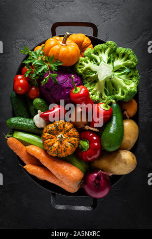 Sfondo culinario con fresche verdure crude su un nero tavolo da cucina, sana alimentazione vegetariana concetto, piatto composizione laici, vista dall'alto Foto Stock