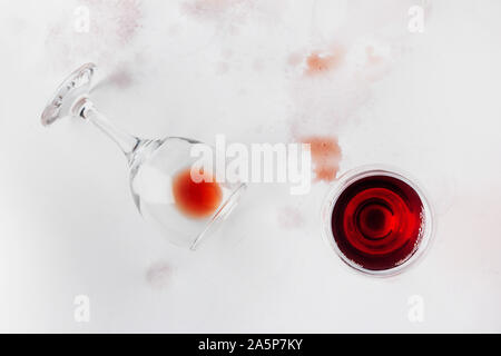 Un bicchiere di vino rosso e un bicchiere rovesciato con i resti di vino su uno sfondo bianco inzuppato e colorate con il vino, vista dall'alto Foto Stock