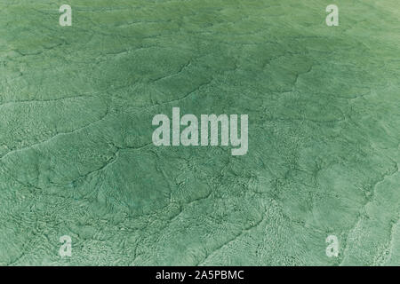 Vuoto astratto naturalmente sullo sfondo creato da piccole onde del mare in acque poco profonde e la luce del sole riflessioni sulla superficie dell'acqua. Tonica in sfumature di verde c Foto Stock