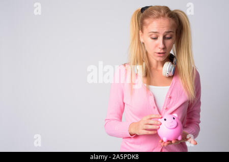 Giovane biondo nerd donna holding salvadanaio e guardando scioccato Foto Stock