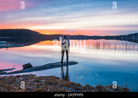 Uomo che guarda un tramonto sul lago Foto Stock