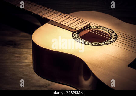 Chitarra acustica che giace su di un tavolo di legno illuminate da un fascio di luce Foto Stock