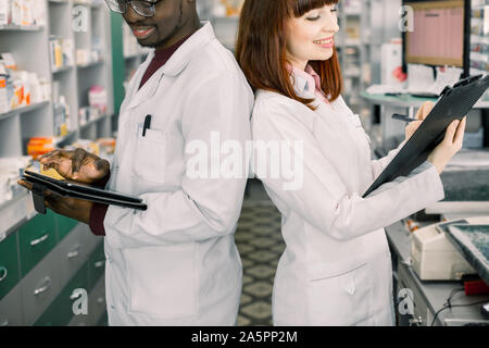 Due multirazziale lavoro farmacisti in farmacia in piedi di schiena. Maschio e femmina farmacisti controllo inventario di medicine in farmacia. Uomo Foto Stock