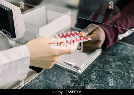 Immagine ritagliata delle mani della donna il farmacista dando red pillole di uomo nero in farmacia Foto Stock