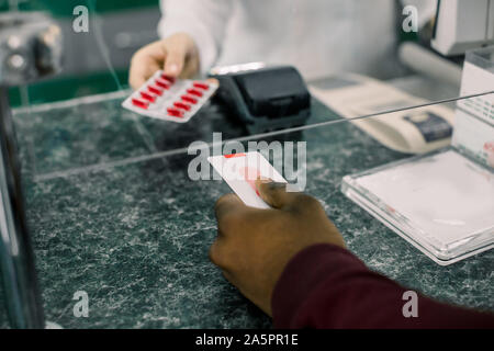 Immagine ritagliata delle mani della donna il farmacista dando red pillole di uomo nero in farmacia. Uomo di pagare per i medicamenti con carta di credito in farmacia Foto Stock