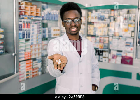 African-medico americano il farmacista uomo azienda e offerta di pillole di bianco. Negozio di droghe e farmaci il concetto di qualità Foto Stock
