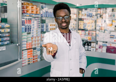 African-medico americano il farmacista uomo azienda e offerta di pillole di bianco. Negozio di droghe e farmaci il concetto di qualità Foto Stock