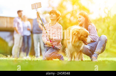 I due ragazzi stanno facendo selfie con selfie stick e cane in giardino in estate Foto Stock